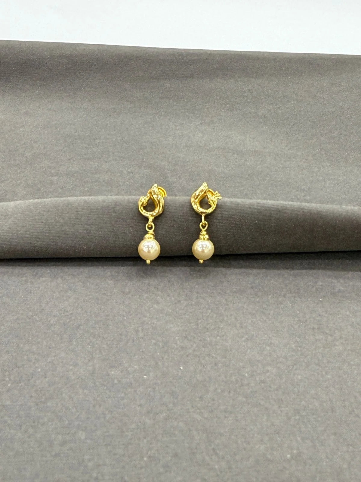 Gold earrings with pearl beads on a gray surface