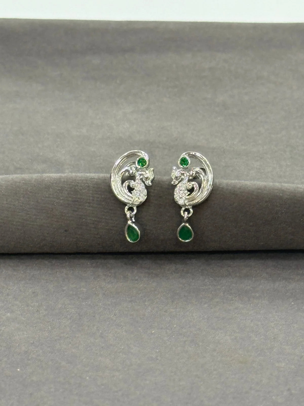 Silver earrings with green gemstones on a gray surface