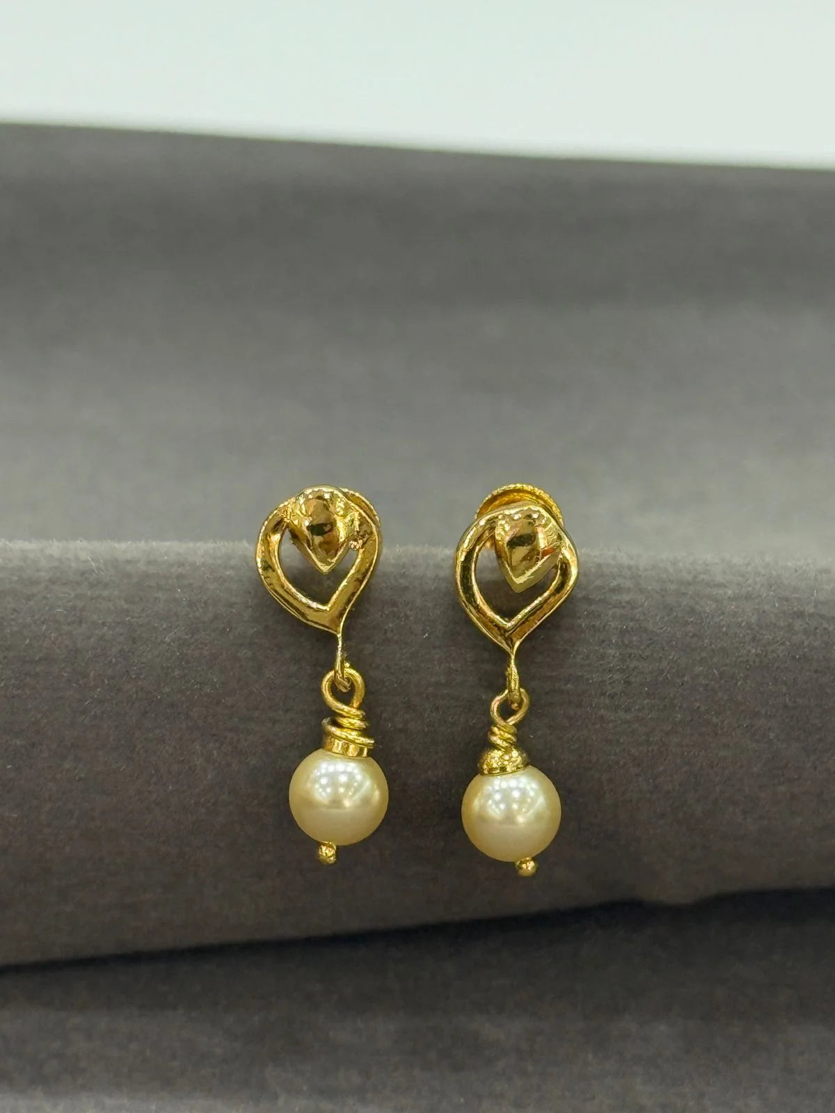 Gold earrings with pearl drops on a gray surface