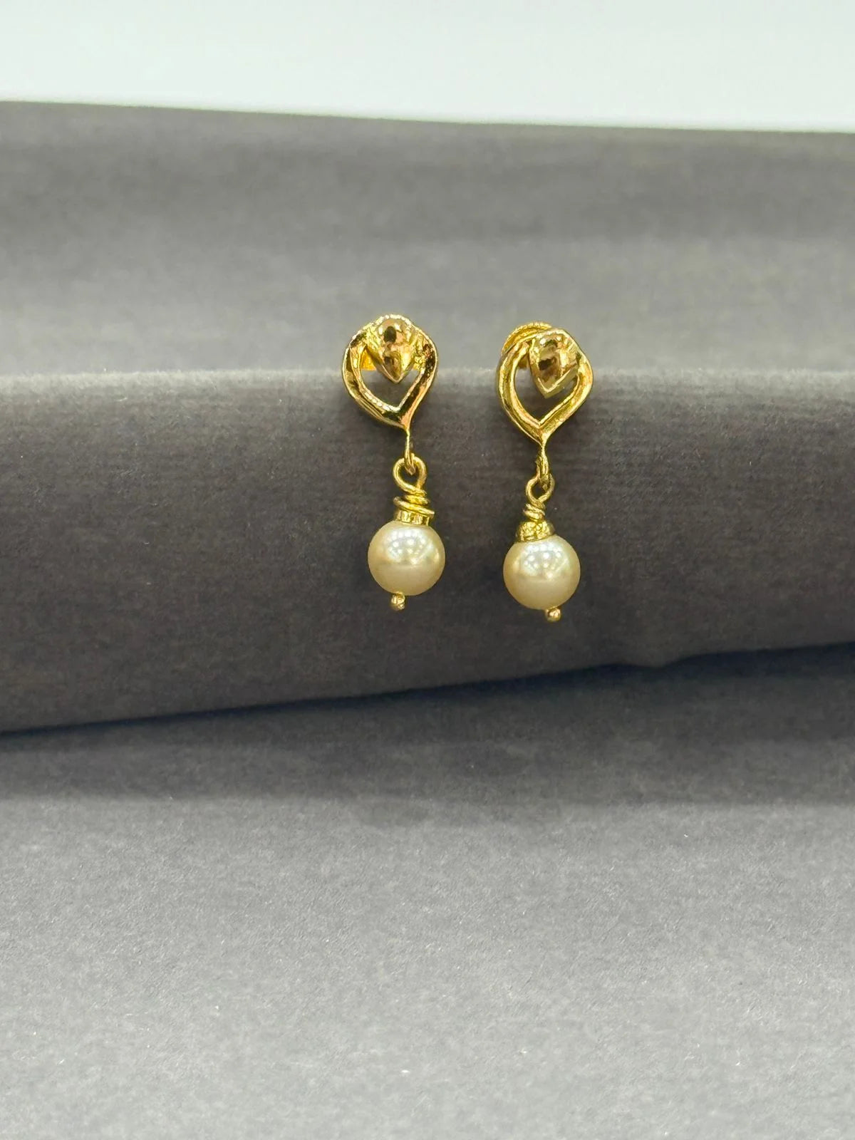 Gold earrings with pearl drops on a gray surface