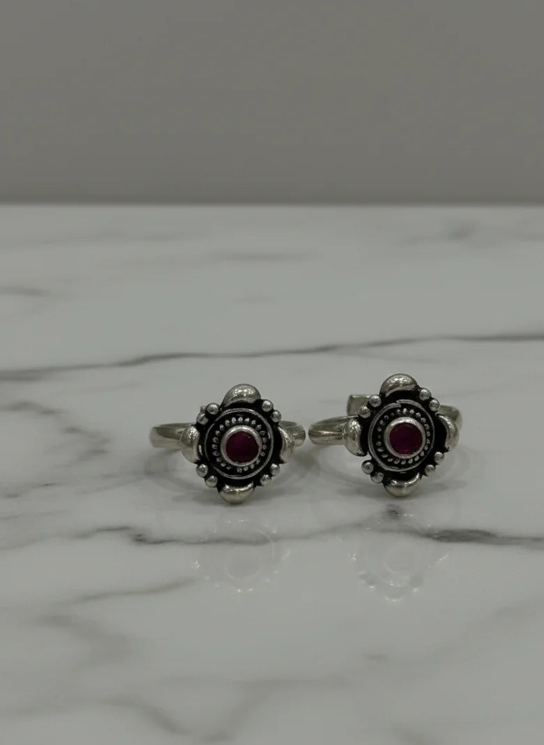 Pair of silver toe  rings with red gemstones on a marble surface