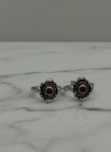 Pair of silver toe  rings with red gemstones on a marble surface