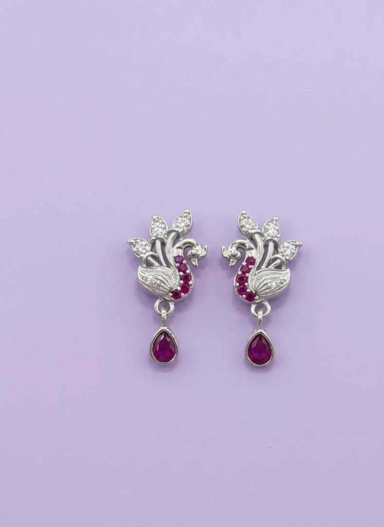 Pair of silver earrings with red gemstones on a purple background