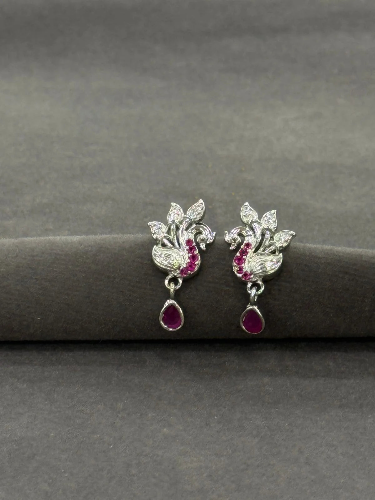 Pair of silver earrings with red gemstones on a gray surface