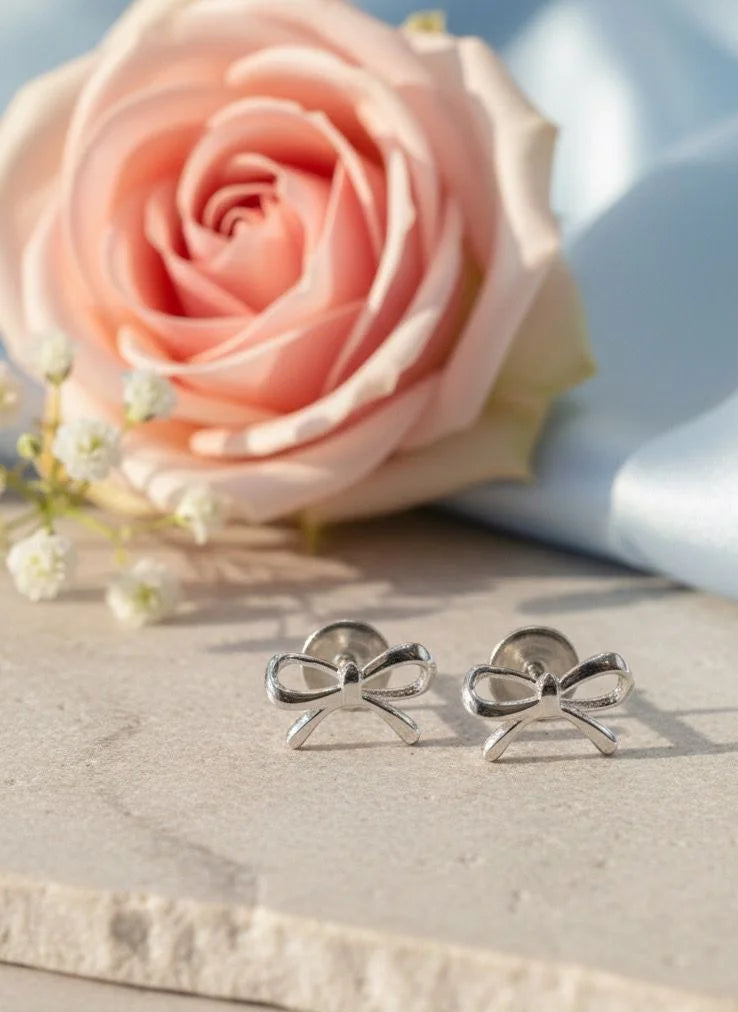 Silver bow-shaped earrings on a marble surface with a pink flower in the background