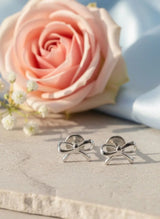Silver bow-shaped earrings on a marble surface with a pink flower in the background
