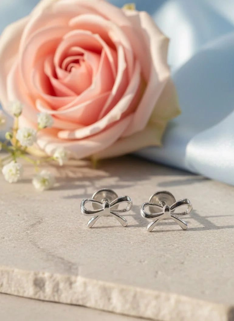 Silver bow-shaped earrings on a marble surface with a pink flower in the background