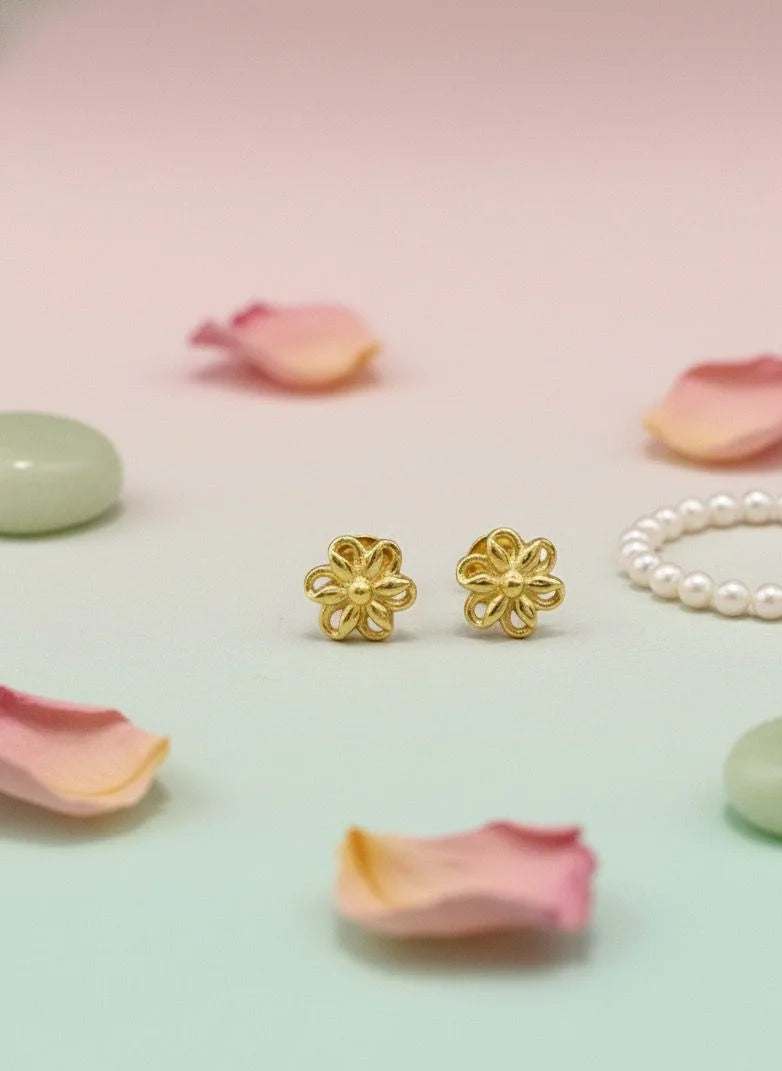 Gold flower-shaped earrings and a pearl bracelet on pink and green stones with scattered rose petals.