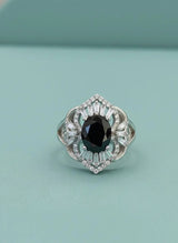 Silver ring with a black gemstone and clear stones on a light blue background