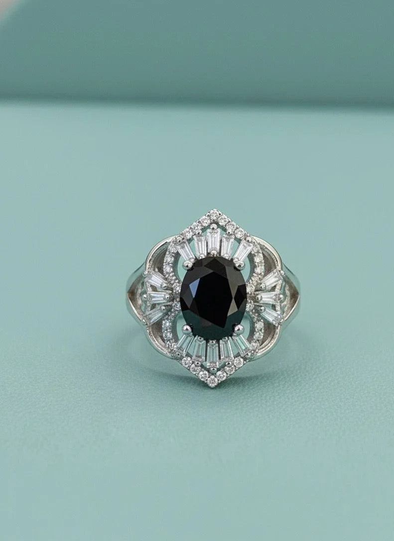 Silver ring with a black gemstone and clear stones on a light blue background