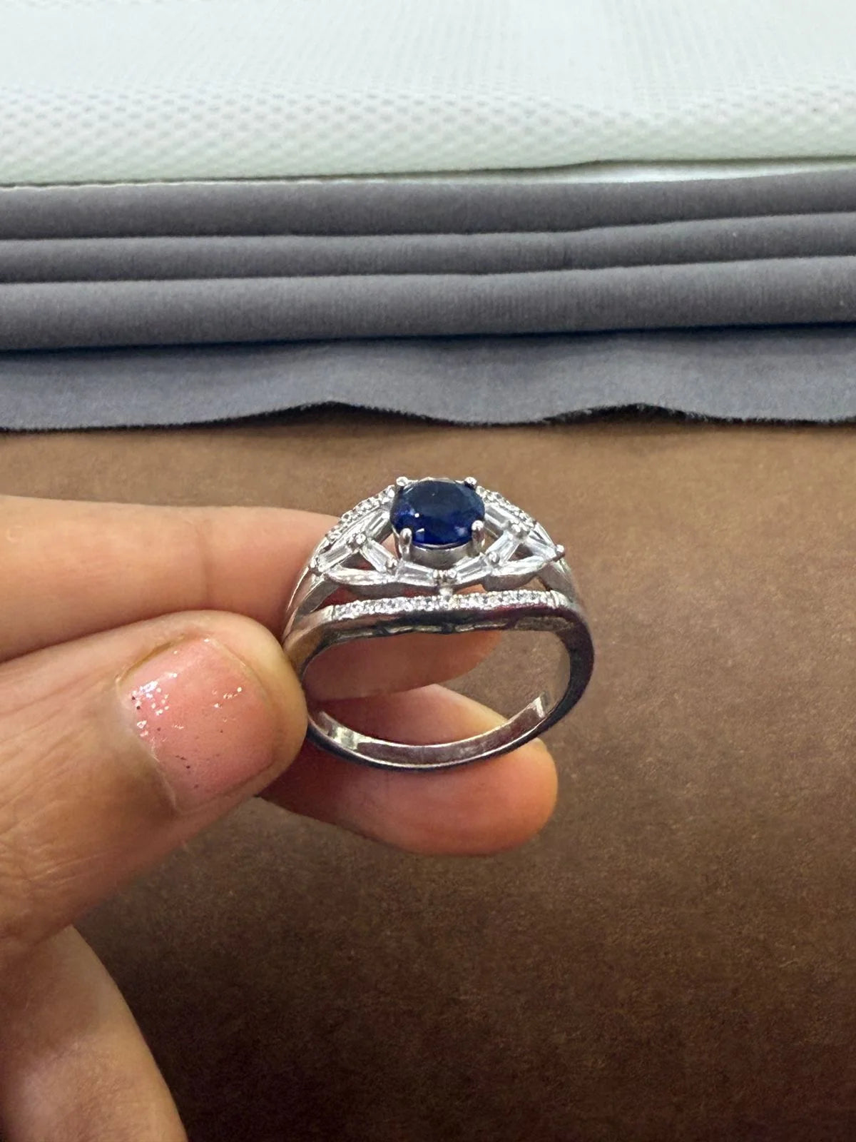 Silver ring with a blue gemstone held by a hand against a fabric background