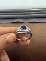Silver ring with a blue gemstone held by a hand against a fabric background