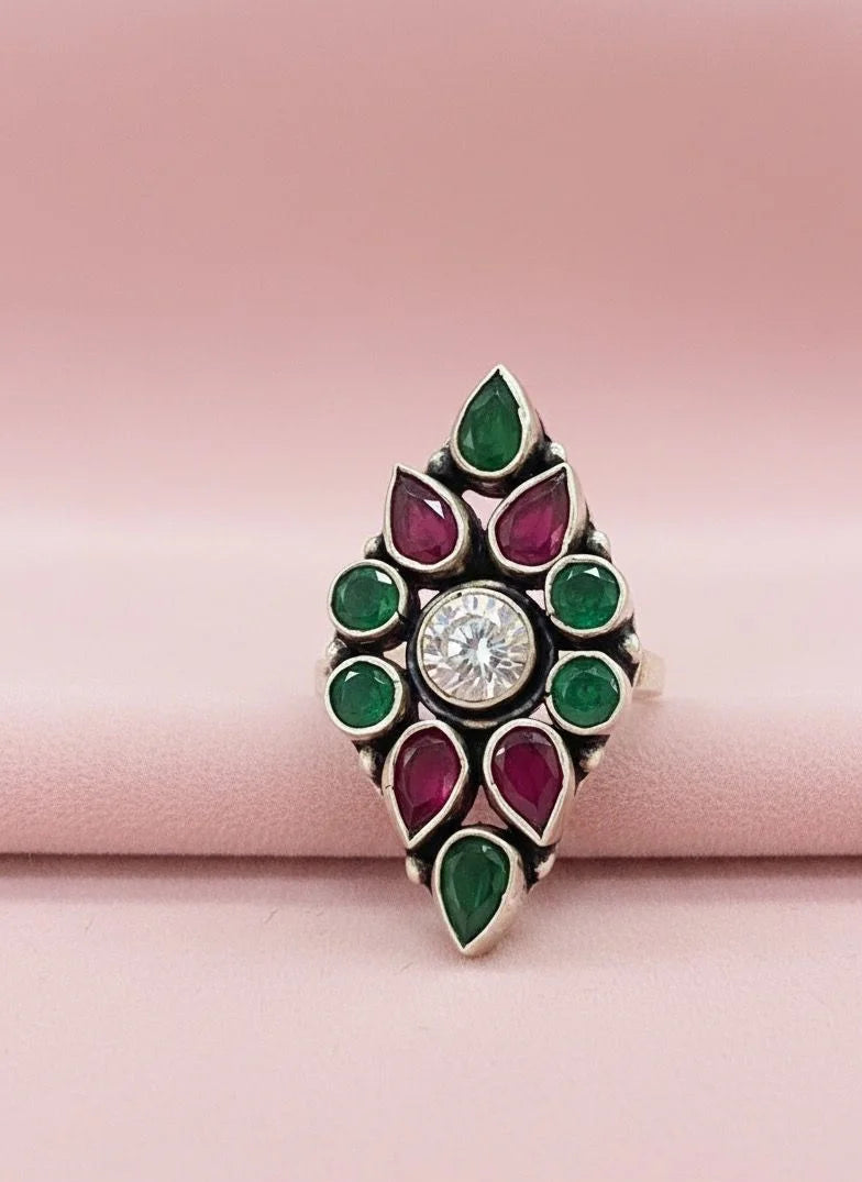 Decorative ring with green and red gemstones on a pink background