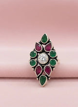 Decorative ring with green and red gemstones on a pink background