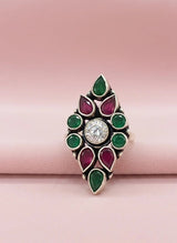 Decorative ring with green and red gemstones on a pink background
