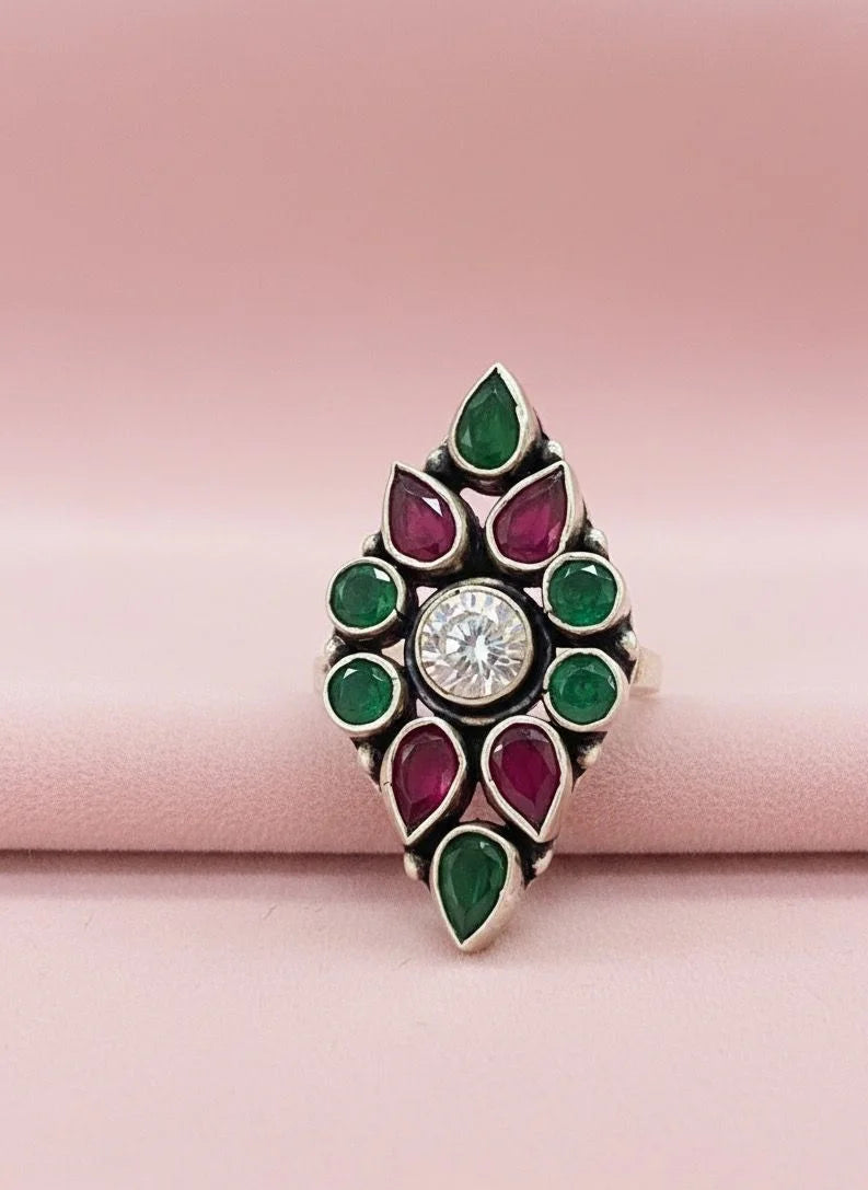 Decorative ring with green and red gemstones on a pink background