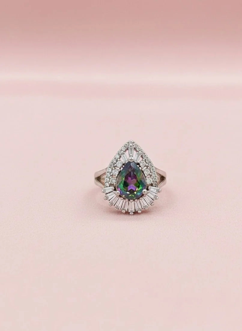 Teardrop-shaped gemstone ring with diamond halo on a pink background