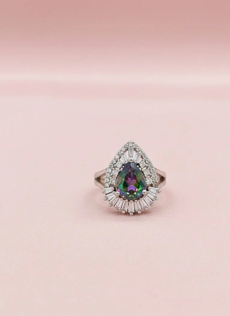 Teardrop-shaped gemstone ring with diamond halo on a pink background