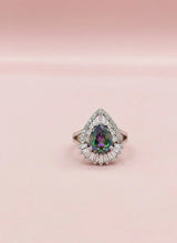 Teardrop-shaped gemstone ring with diamond halo on a pink background