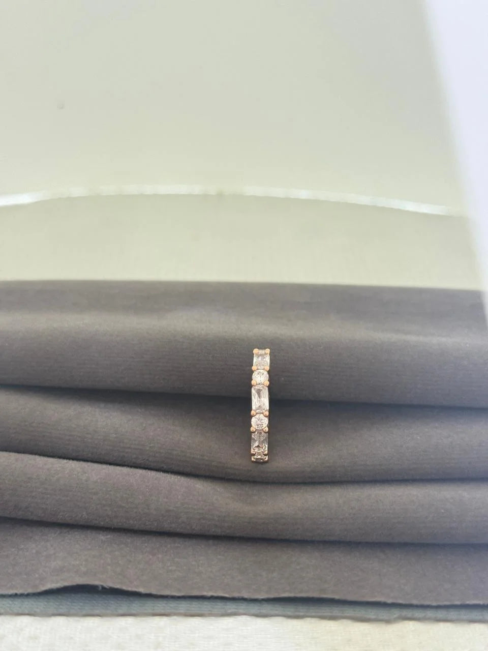 Rose gold ring with small diamonds on a stack of gray fabric