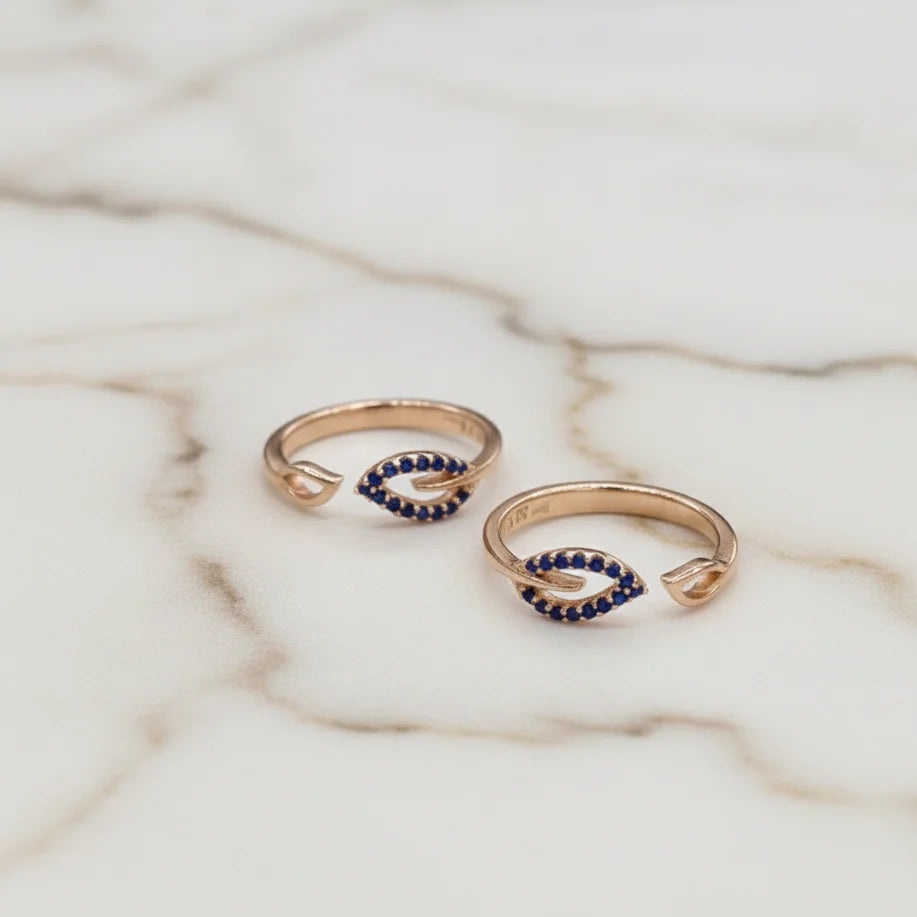 Two gold toe rings with blue gemstones on a marble surface