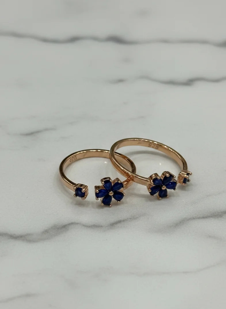 Two gold toe rings with blue gemstones on a marble surface