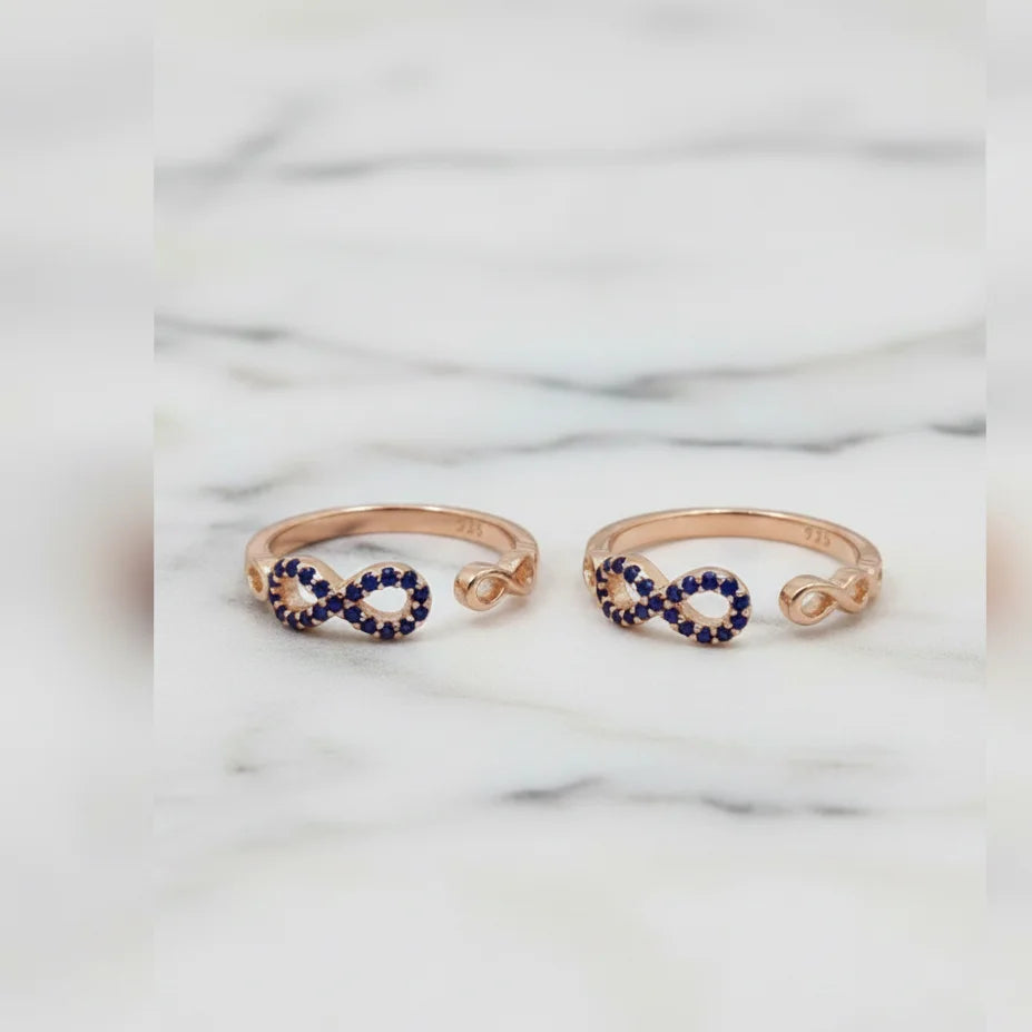 Two rose gold toe  rings with blue gemstones on a marble background