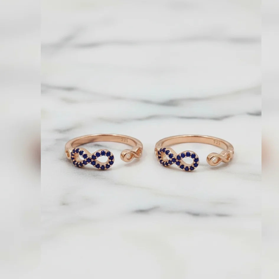 Rose gold infinity toe rings with blue gemstones on a marble background