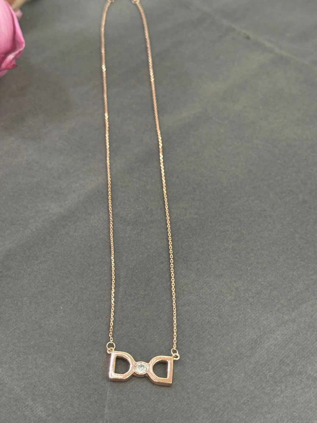 Gold bow-shaped necklace with a small diamond on a gray surface