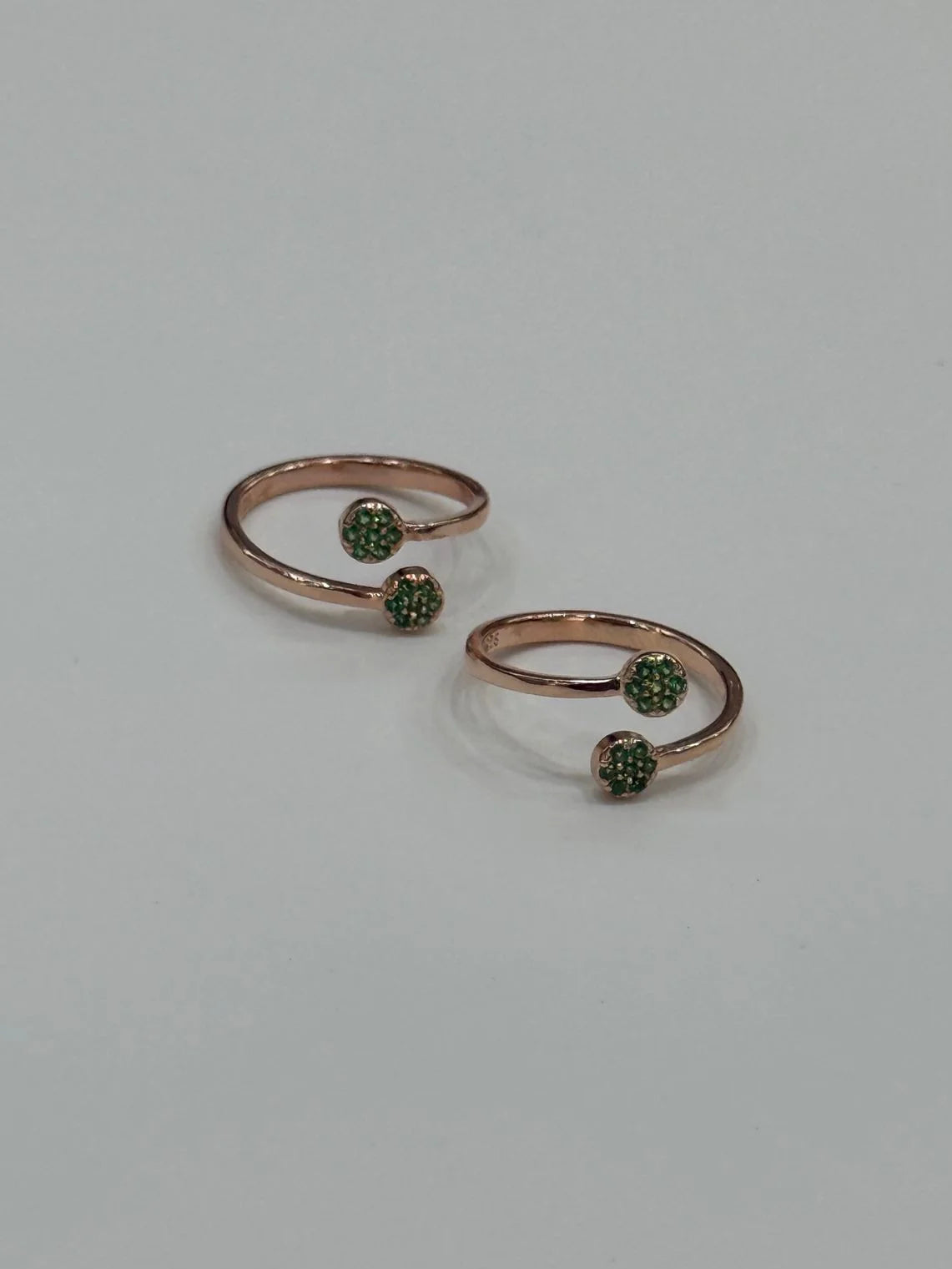 Two rose gold toe rings with green gemstones on a light gray background