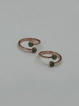 Two rose gold toe rings with green gemstones on a light gray background