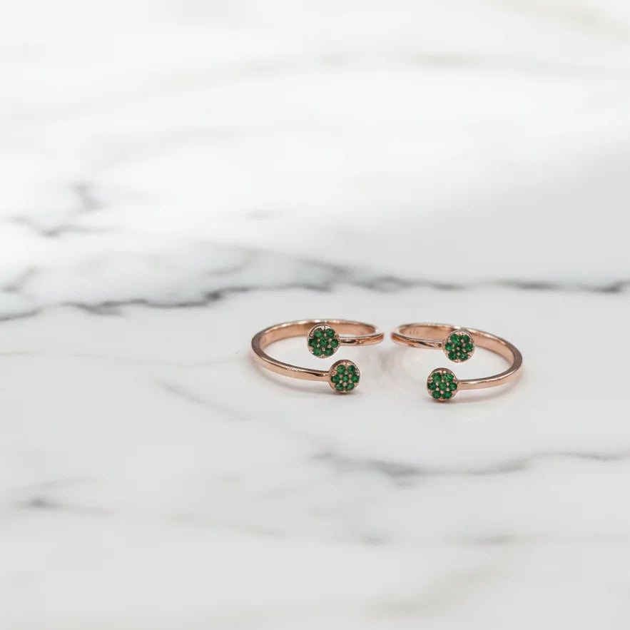 Rose gold toe rings with green gemstones on a marble background