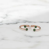 Rose gold toe rings with green gemstones on a marble background