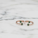 Rose gold toe ring with green gemstones on a marble background