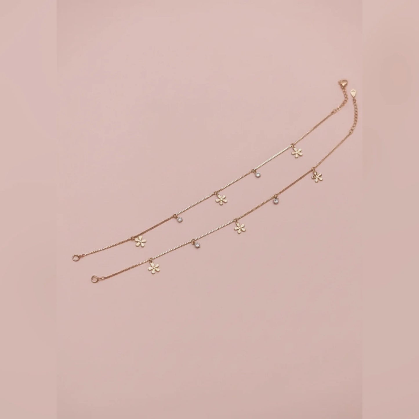 Gold anklet with floral pendants on a pink background
