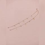 Gold anklet with floral pendants on a pink background