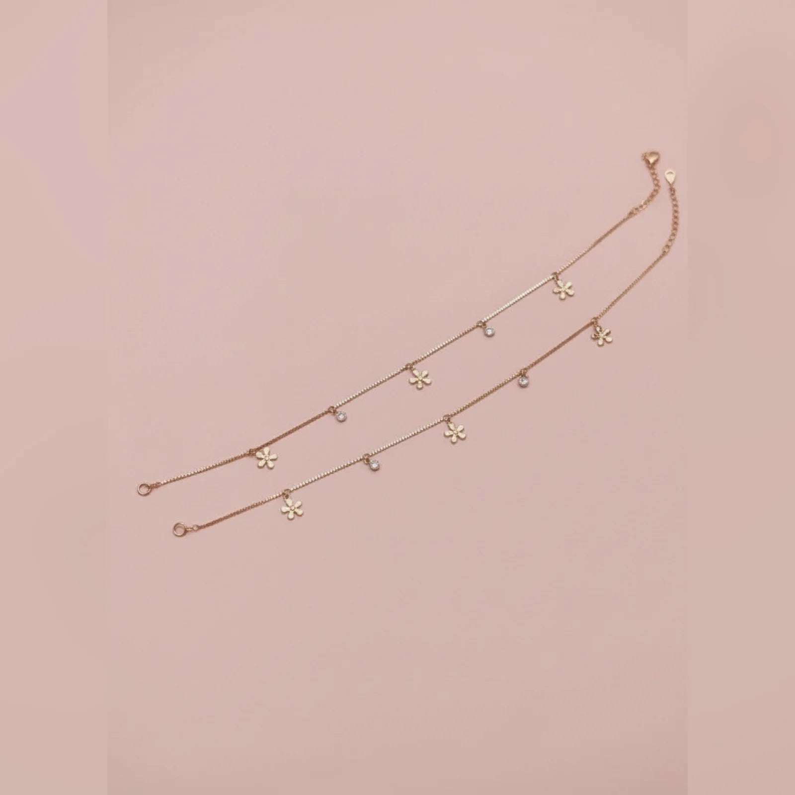 Gold anklet with floral pendants on a pink background