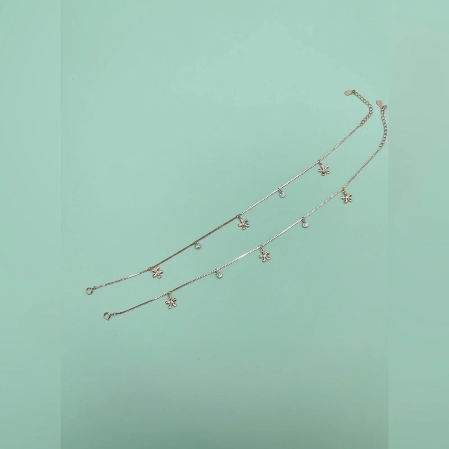 Gold anklet with small charms on a light green background