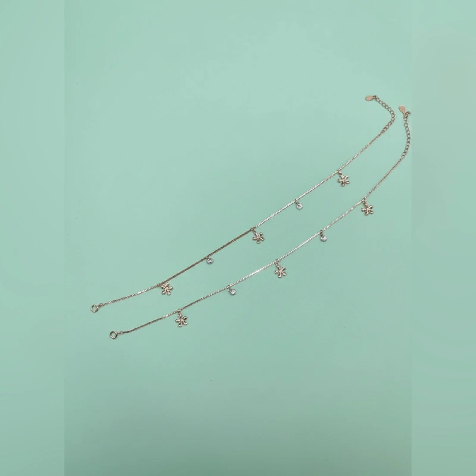 Gold anklet with small charms on a light green background