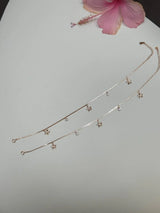 Silver anklet with floral pendants on a light gray background with a pink flower.