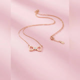 Rose gold bow-shaped necklace on a pink background
