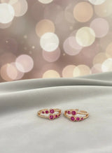 Pair of gold toe rings with red gemstones on a white surface with a blurred bokeh background