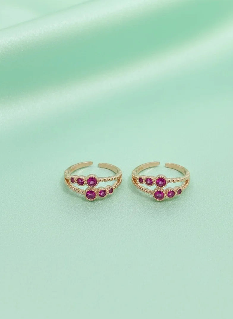 Pair of toe rings with red gemstones on a light green background