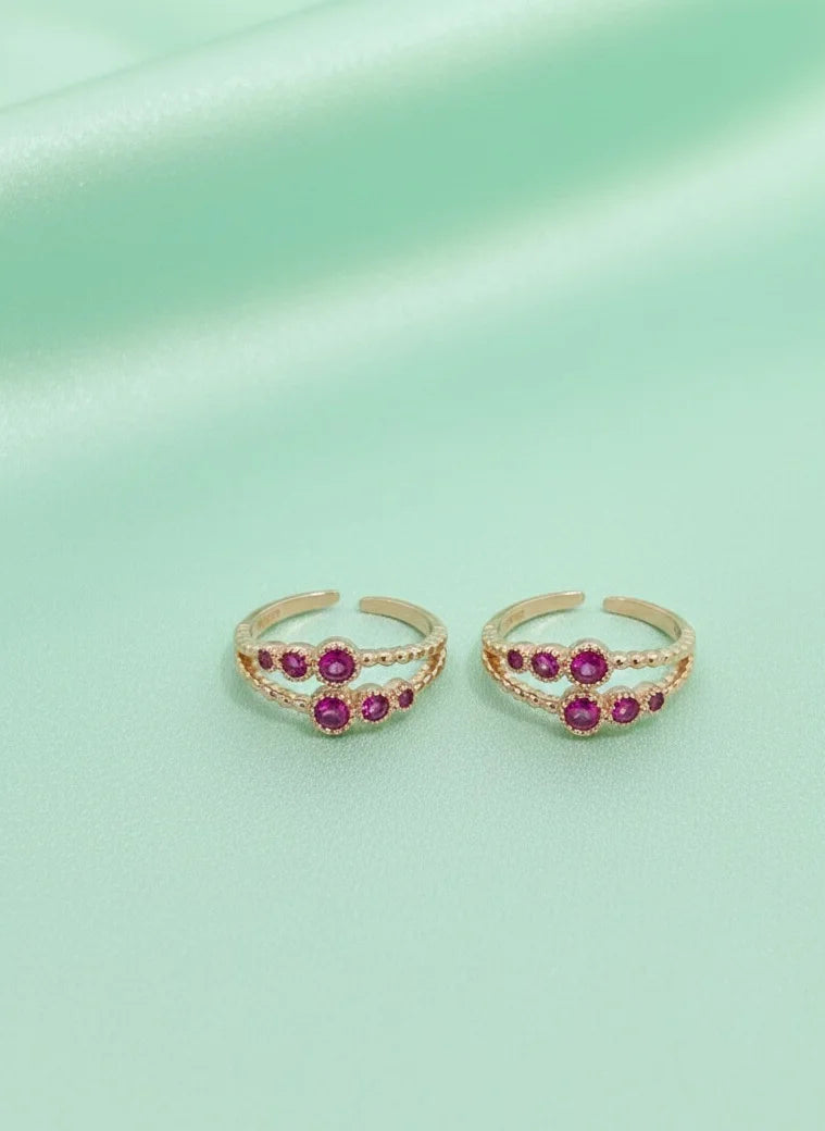 Pair of gold toe rings with red gemstones on a light green background