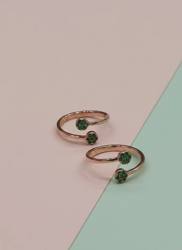 Two rose gold toe rings with green gemstones on a two-tone pink and green background