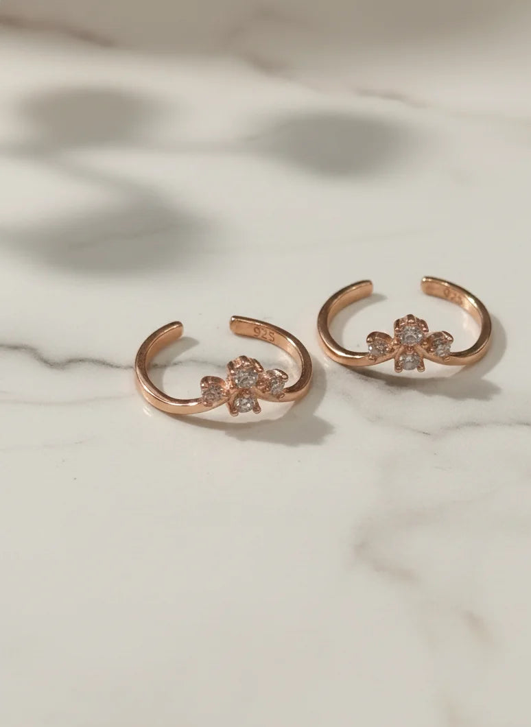 Rose gold toe rings with floral designs on a marble surface