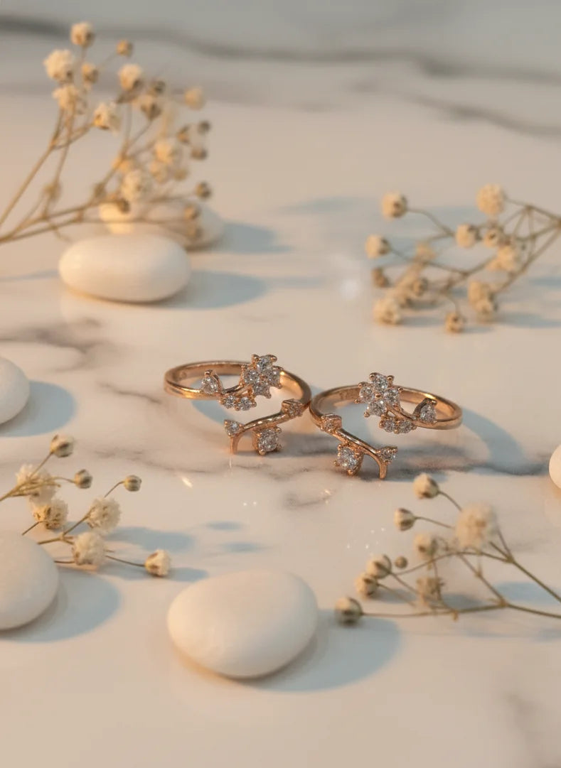 Two gold toe rings with diamond accents on a marble surface with small white flowers.