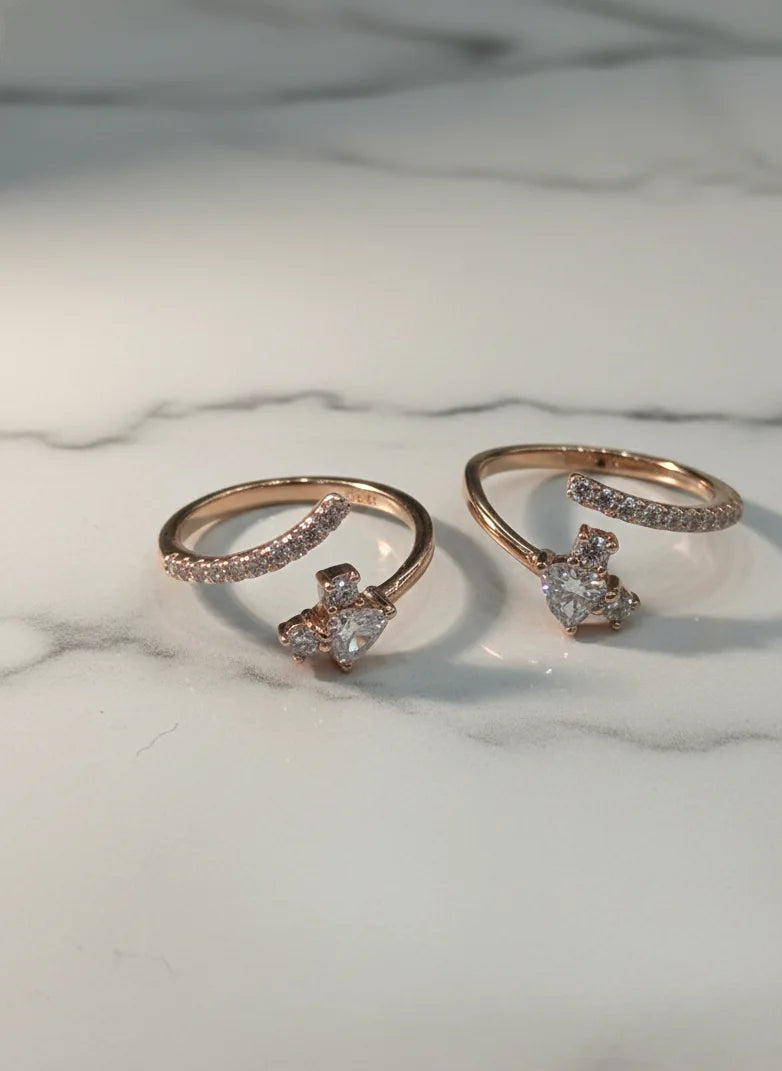Two rose gold toe rings with heart-shaped gemstones on a marble surface