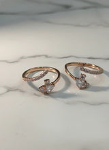 Two rose gold toe rings with heart-shaped gemstones on a marble surface