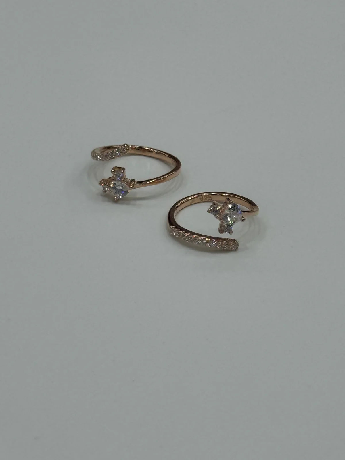 Pair of rose gold toe rings with small diamonds on a light gray background